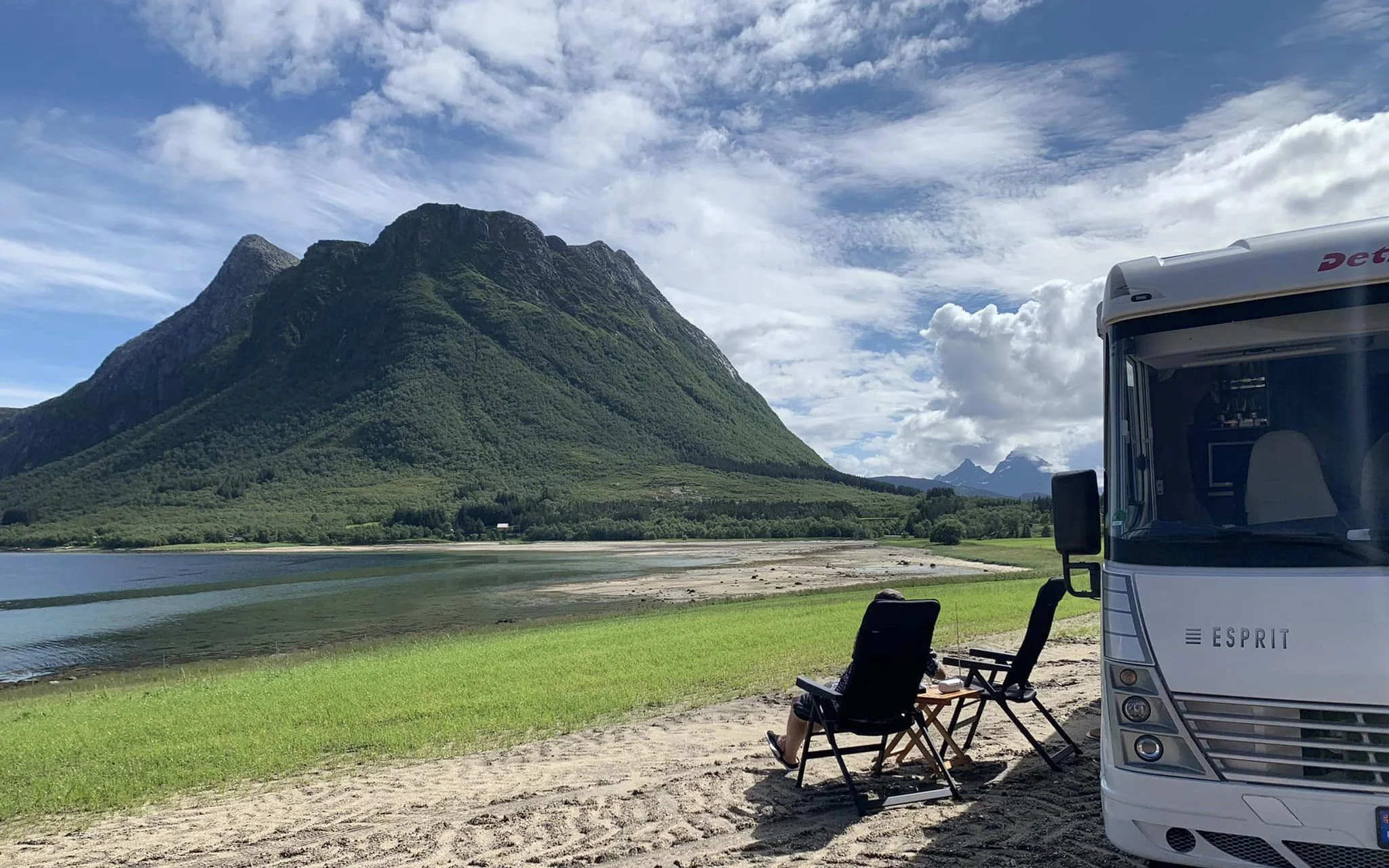 View of a motorhome parked near a scenic beach with towering green mountains in Norway